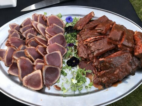 A platter with slices of seared tuna on the left and BBQ beef brisket on the right, garnished with greens and flowers.